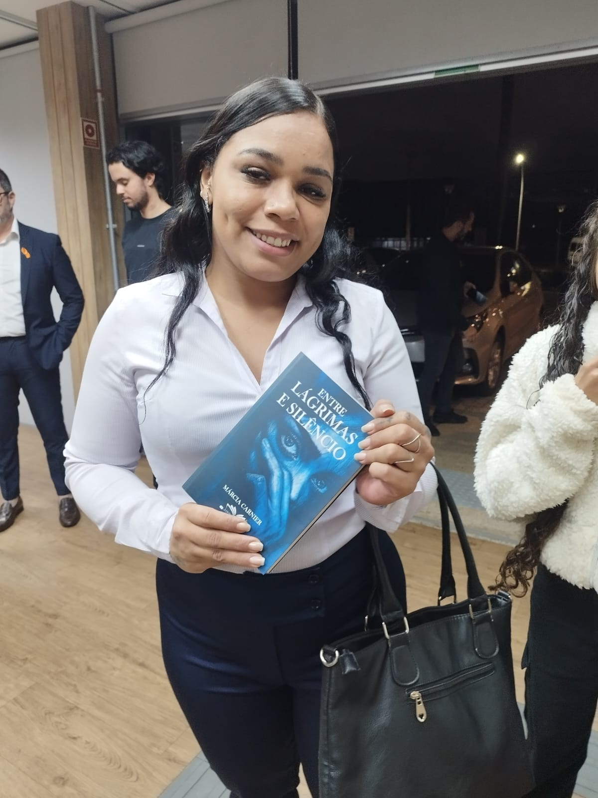 Mulher sorrindo com o livro Entre Lágrimas e Silêncio nas mãos